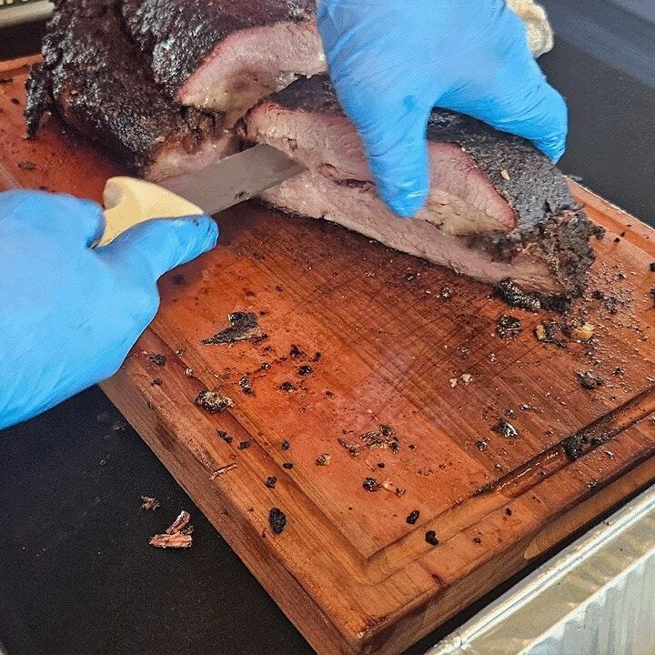 Jim slicing pit smoked brisket on a wooden board, showing the smoke ring